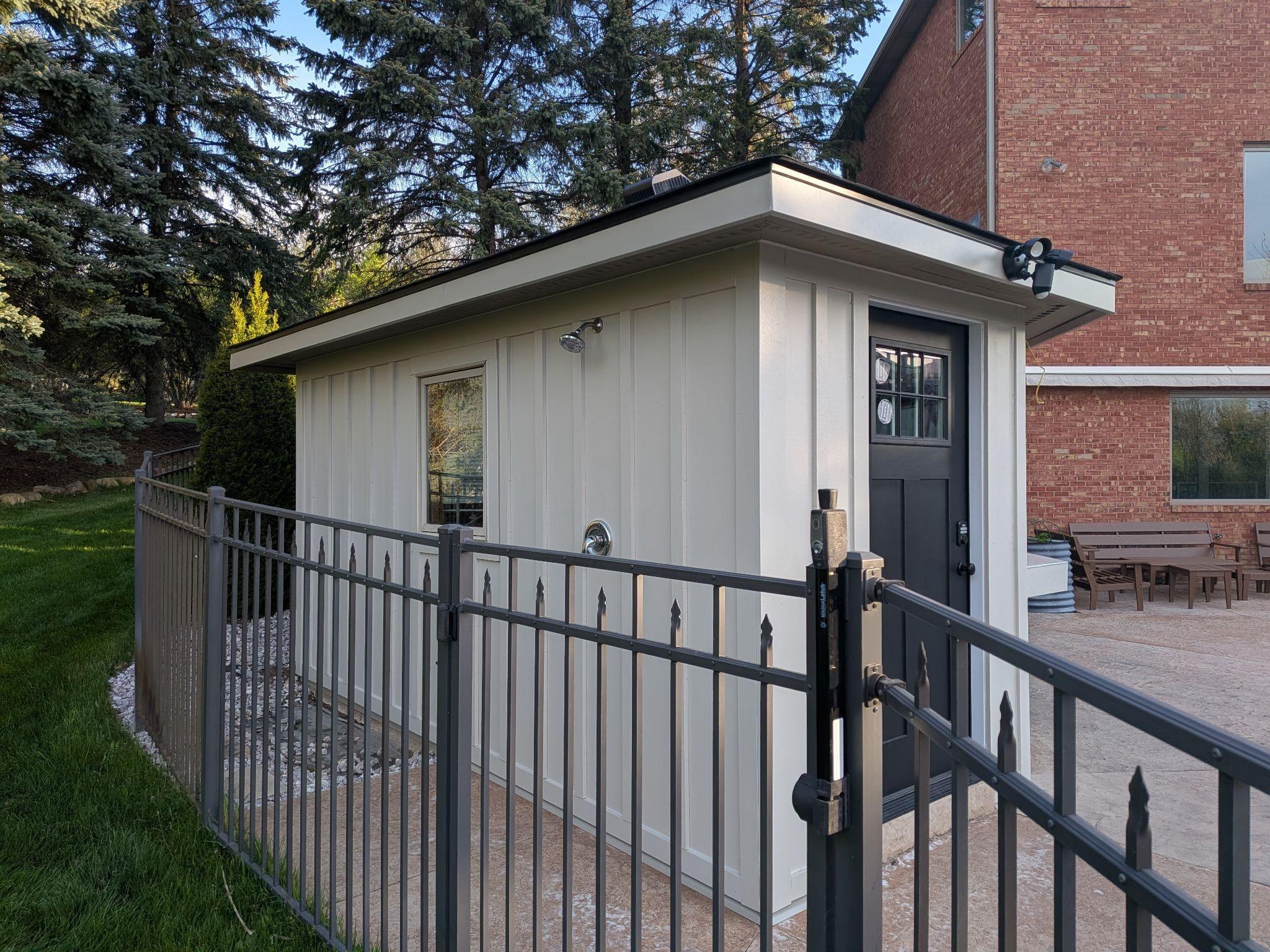 Front of a re-sided pool house with a new black glass door and sconces