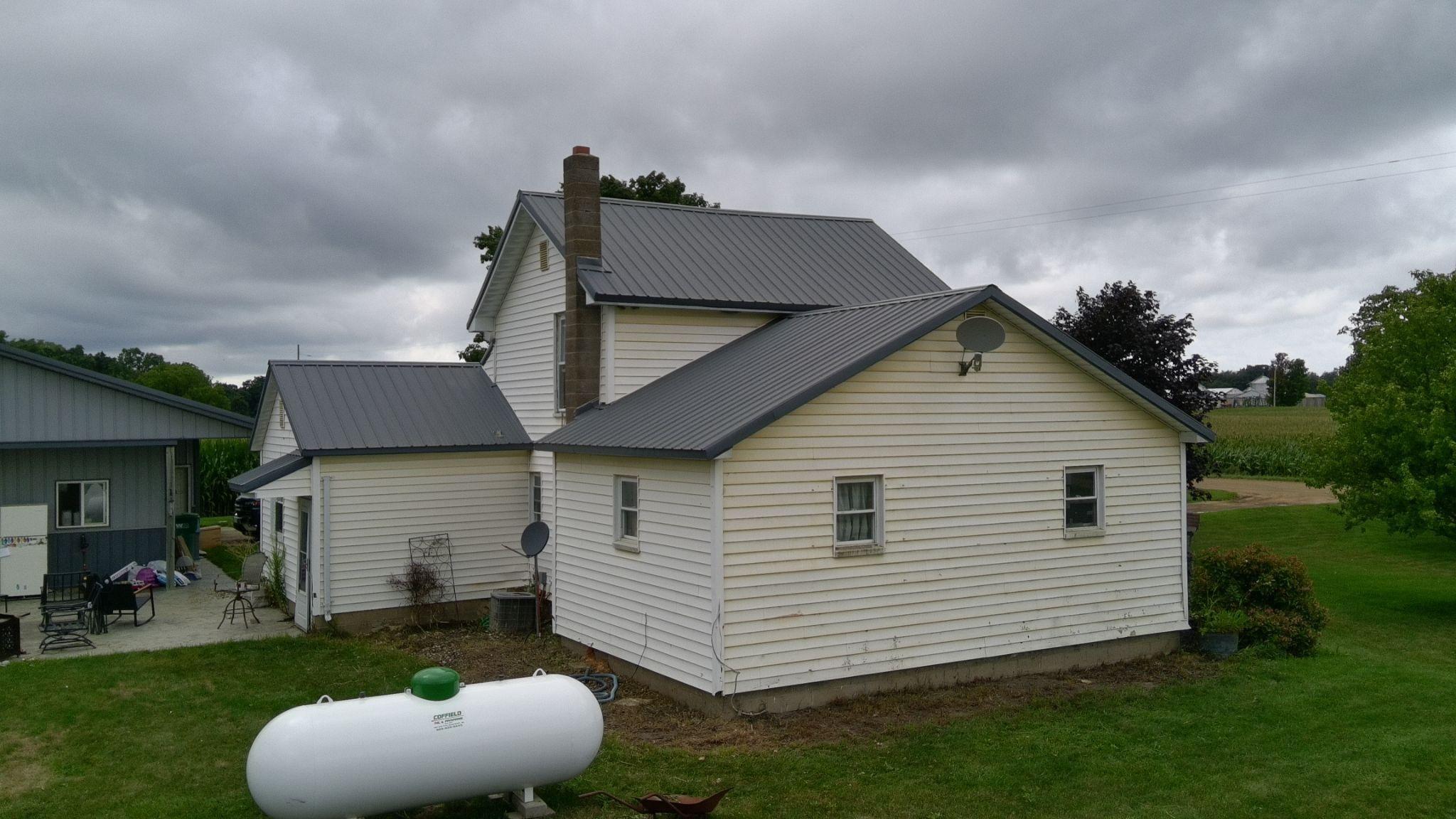 A white farmhouse with a metal roof seen from the side, with a propane tank in the yard