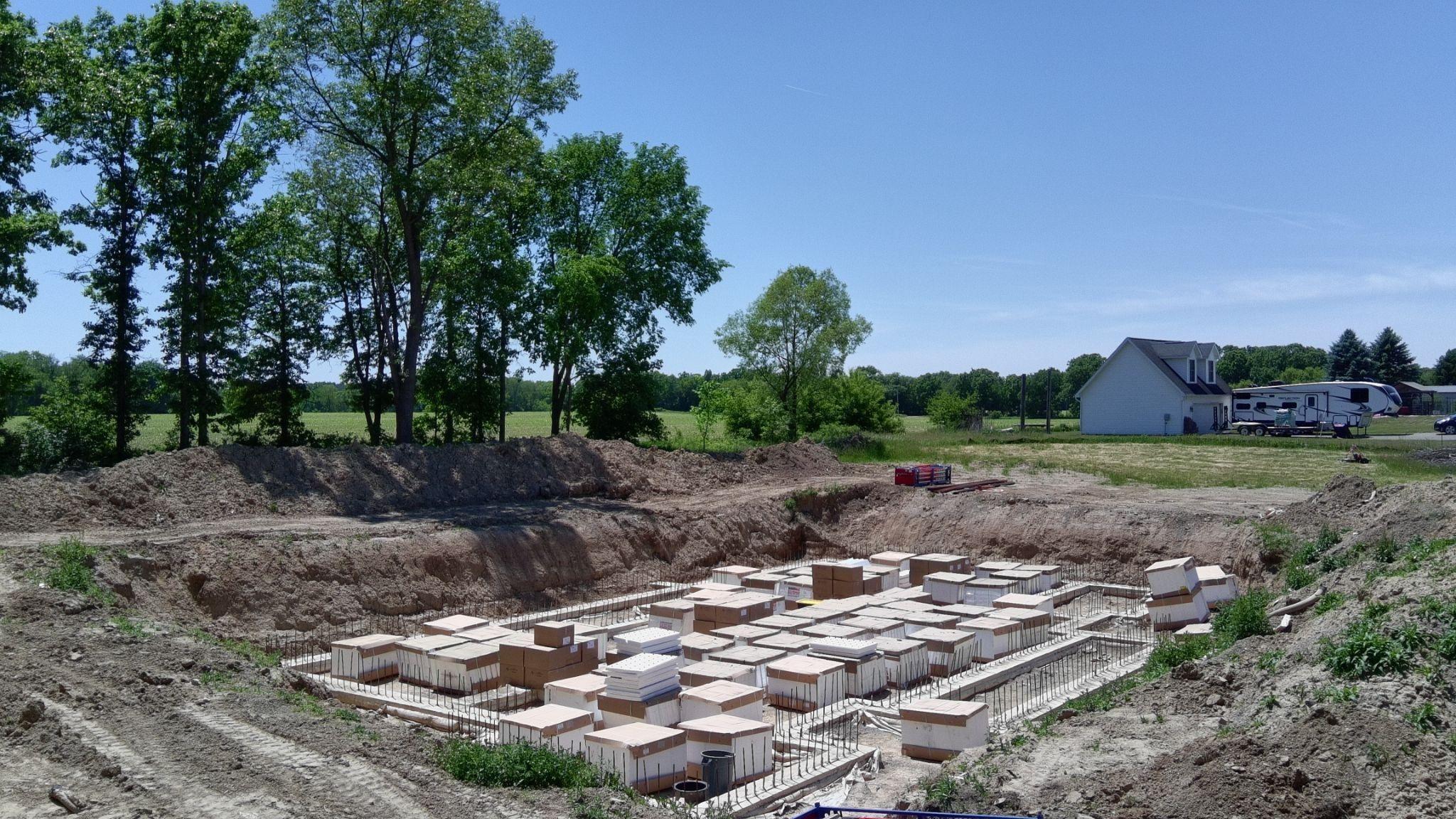 An excavated building site with pallets of white ICF blocks stacked on the footings