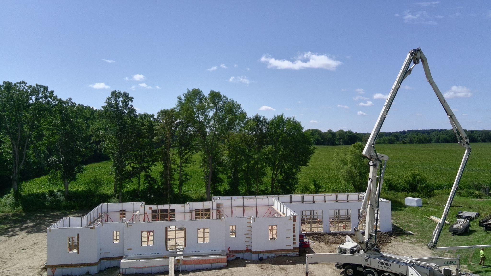 A pump truck boom over ICF walls with a farm field and trees beyond