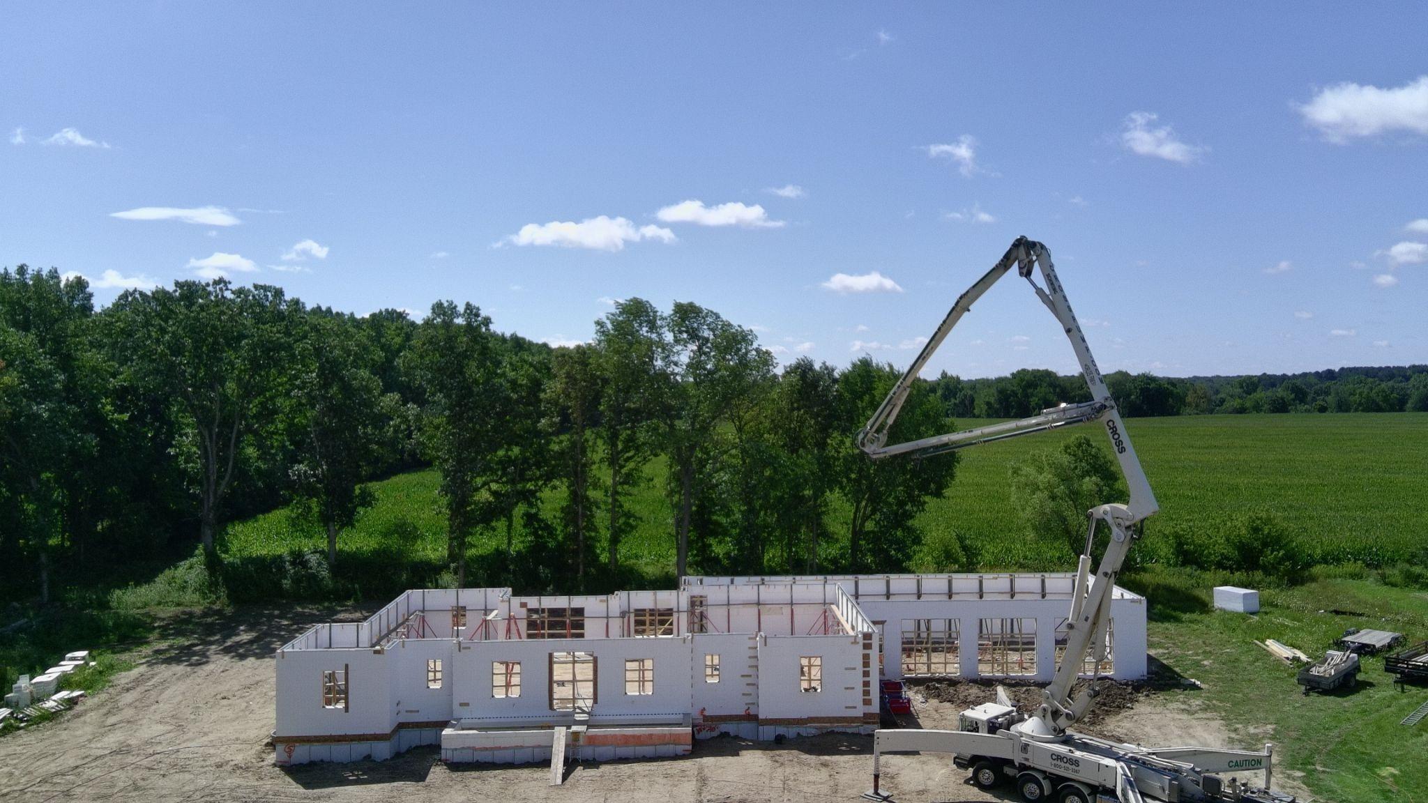 A concrete pump boom folded high over a single-story ICF wall shell beside a green field