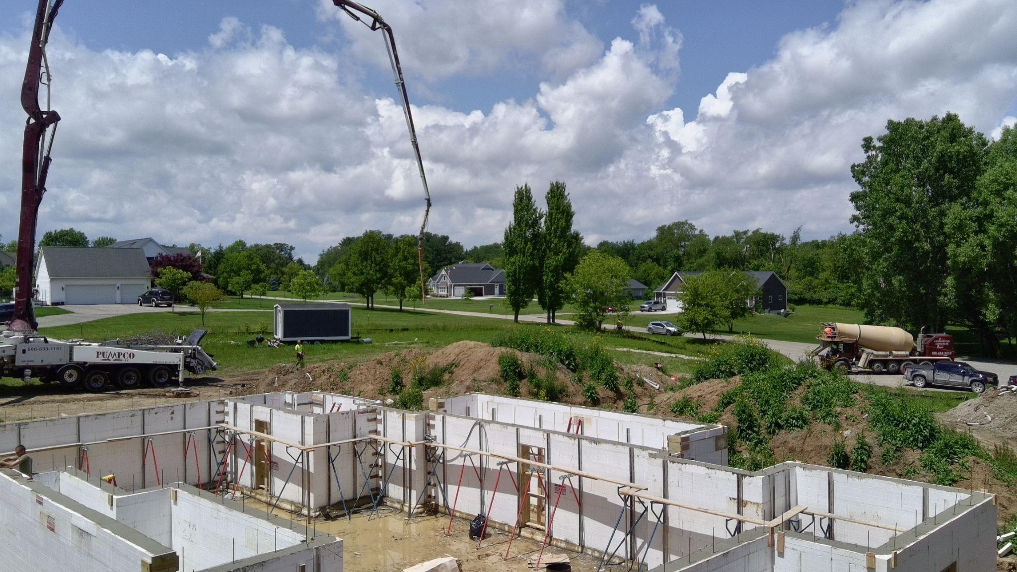 A concrete pump boom over white ICF walls with houses in the background