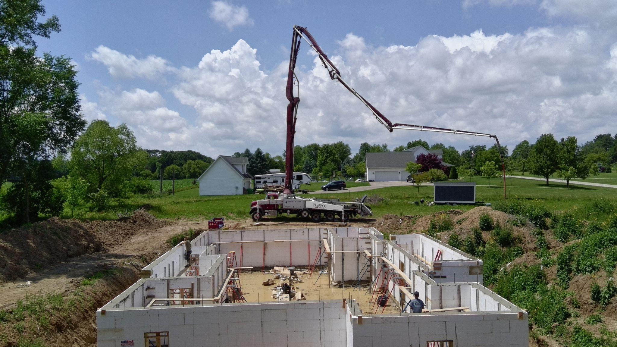 A concrete pump truck boom arching over ICF foundation walls under a blue sky with clouds