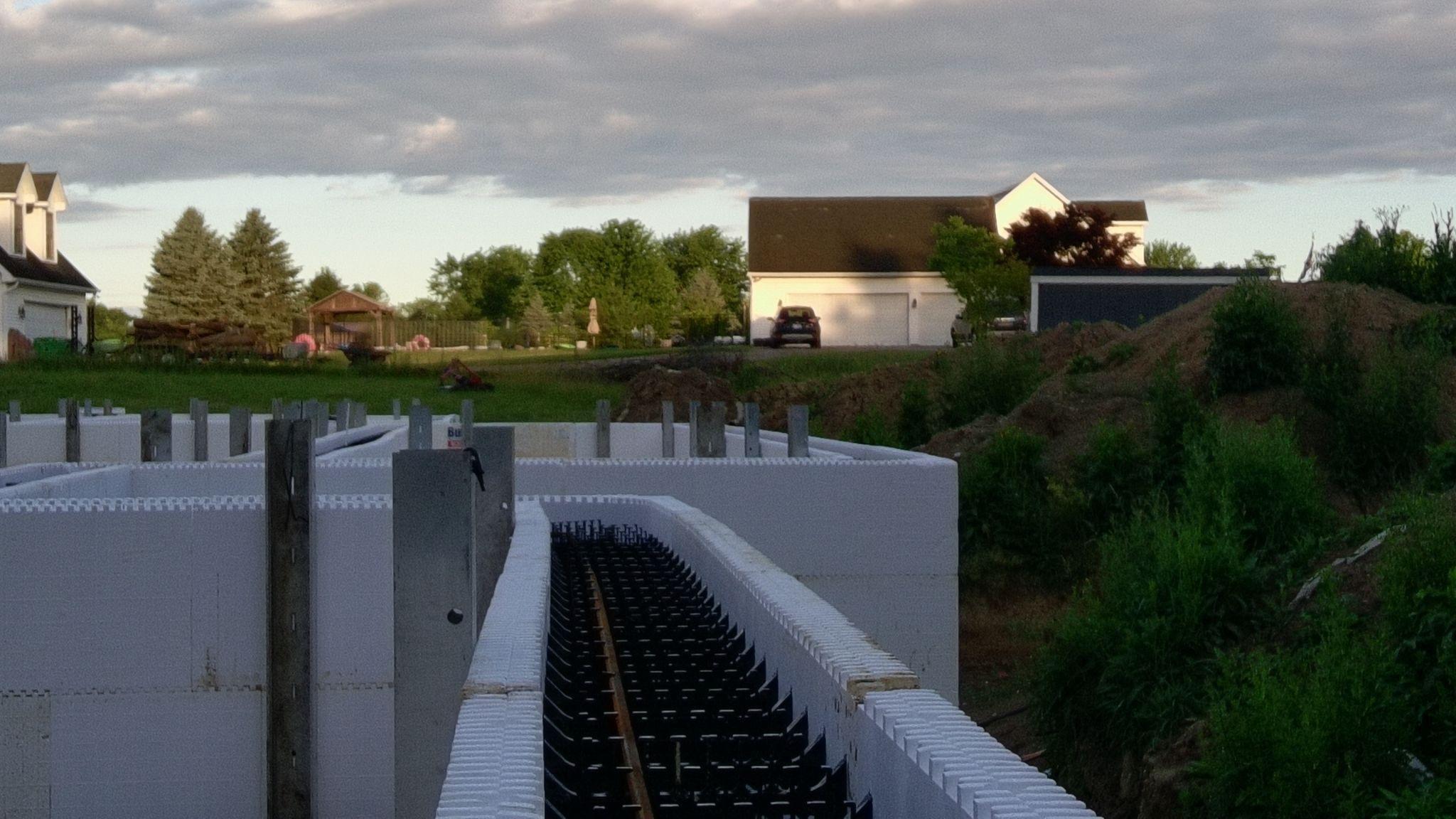 Close-up looking down into an ICF wall cavity showing black plastic web ties and a horizontal rebar rod between the foam faces