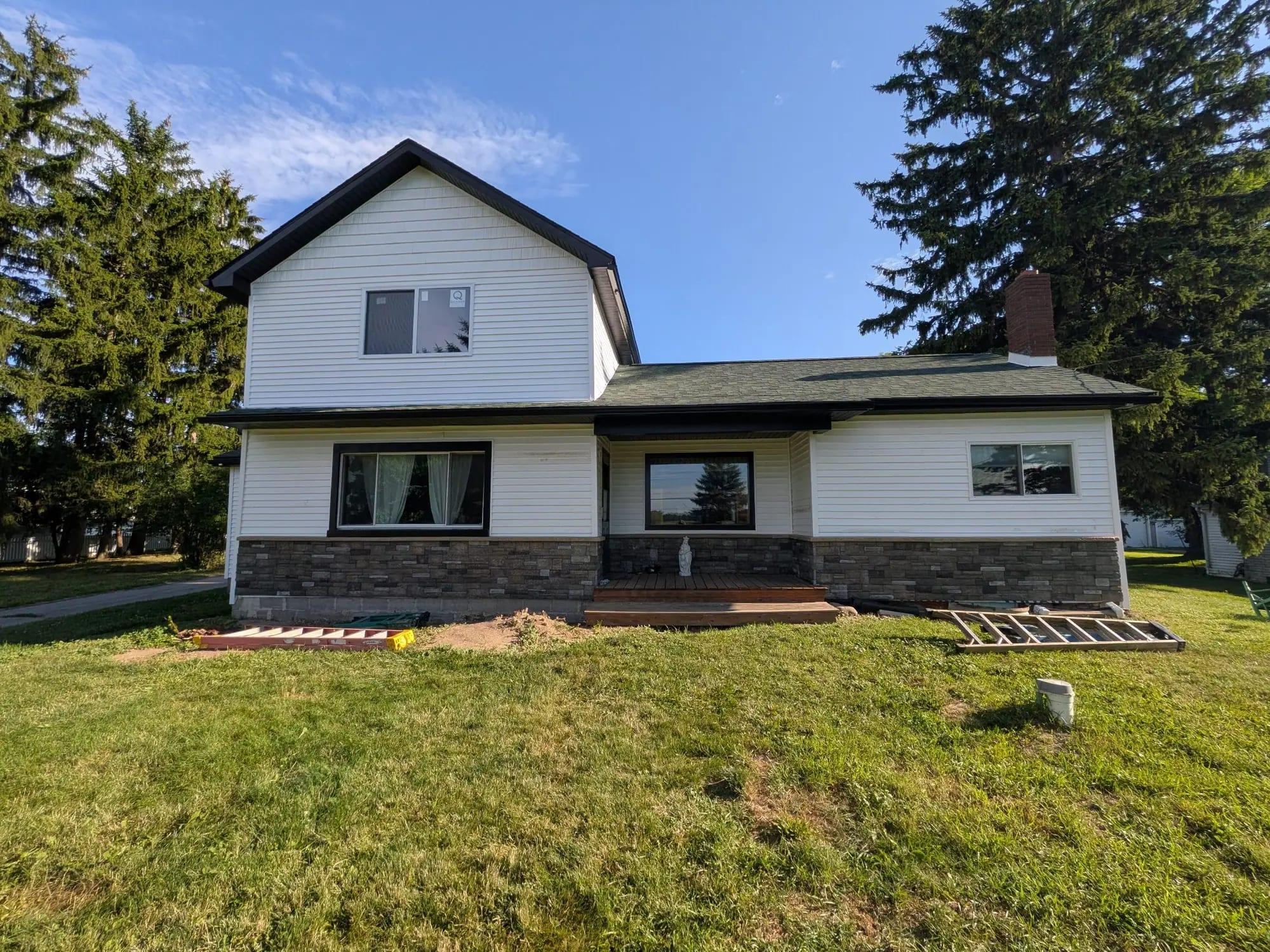 A two-story house with new white siding, black trim, stone veneer and a covered porch