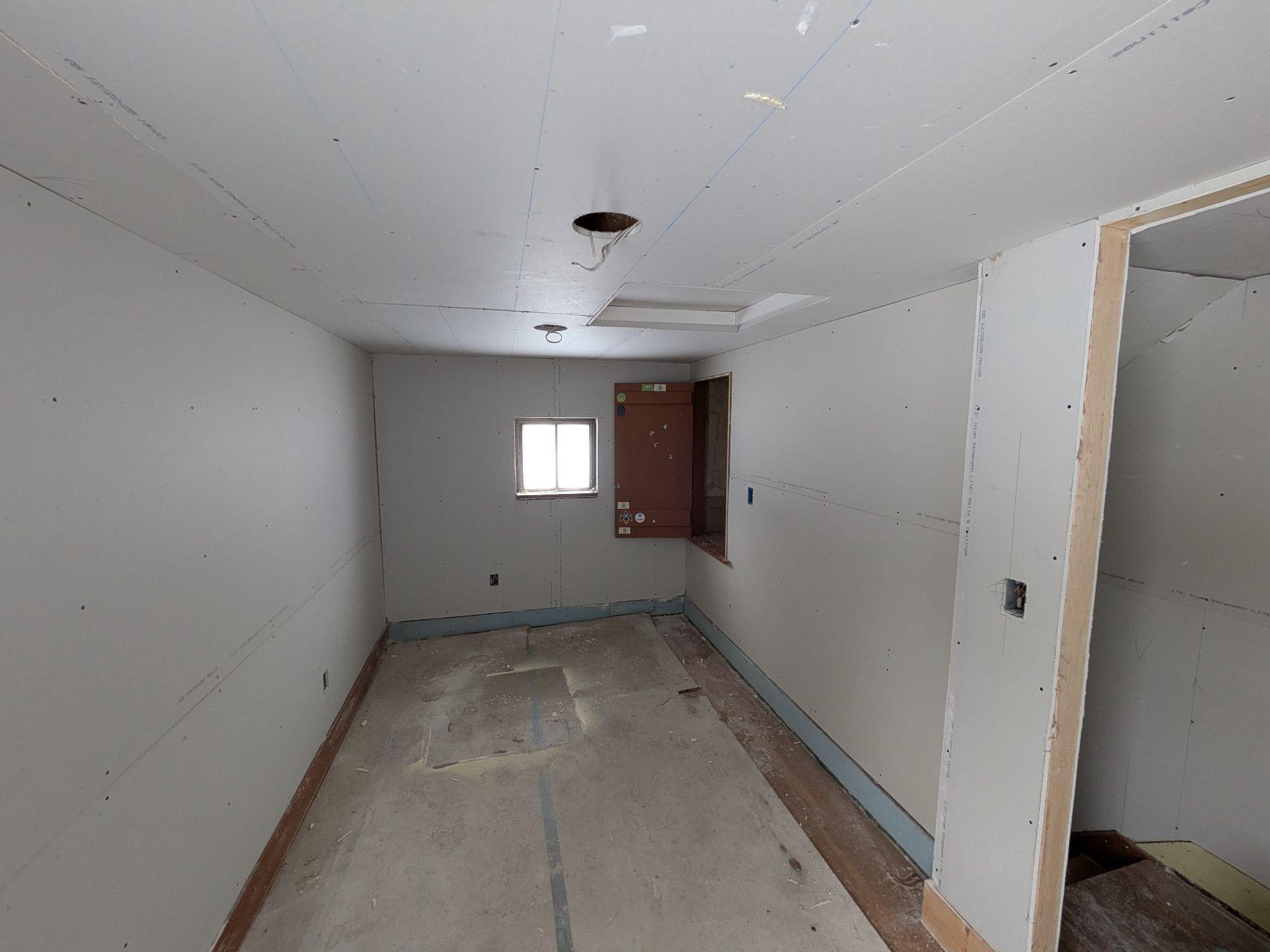 A room with new drywall hung and taped, a new window and door