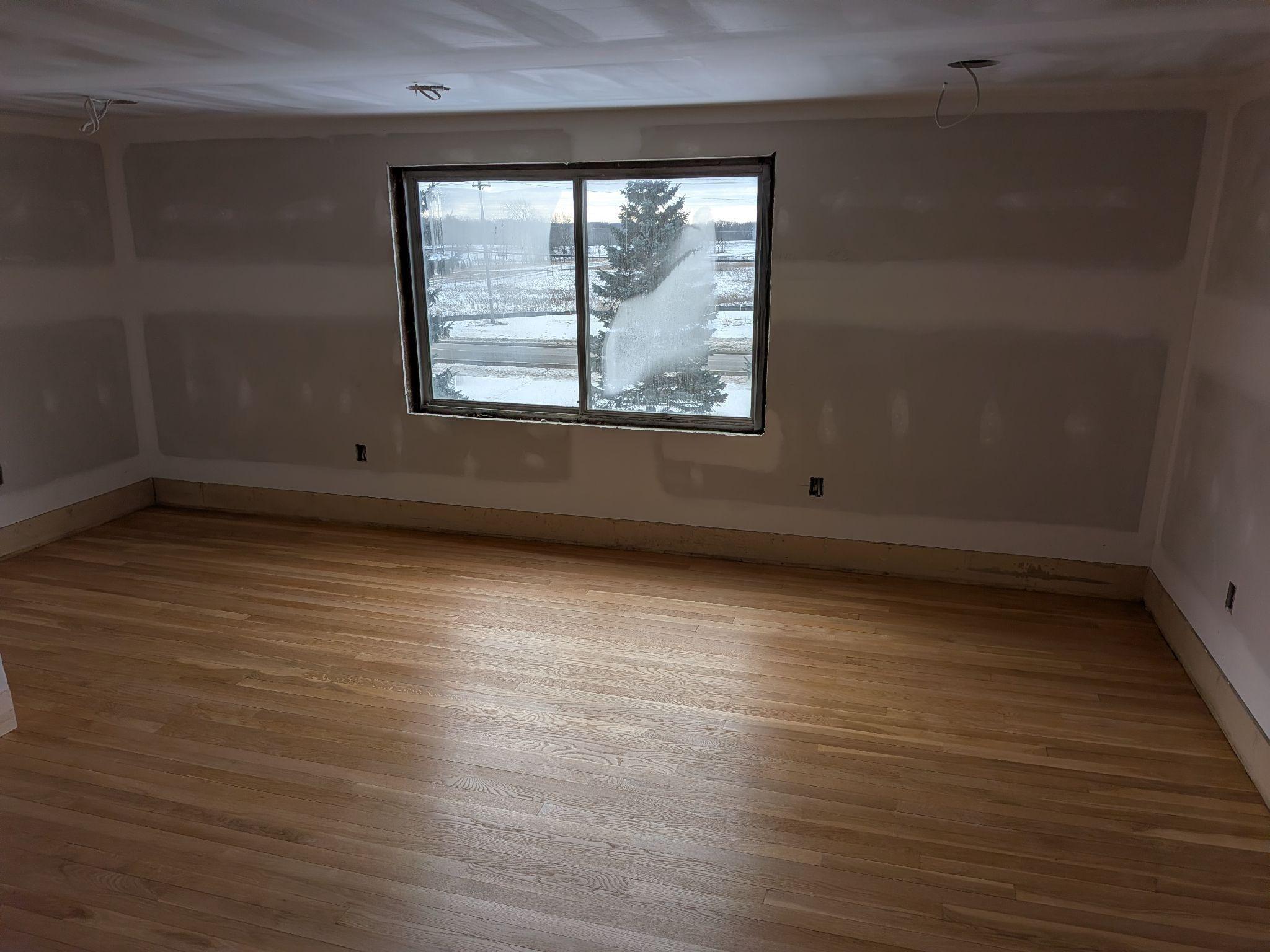 A bright room with finished drywall and warm wood floors
