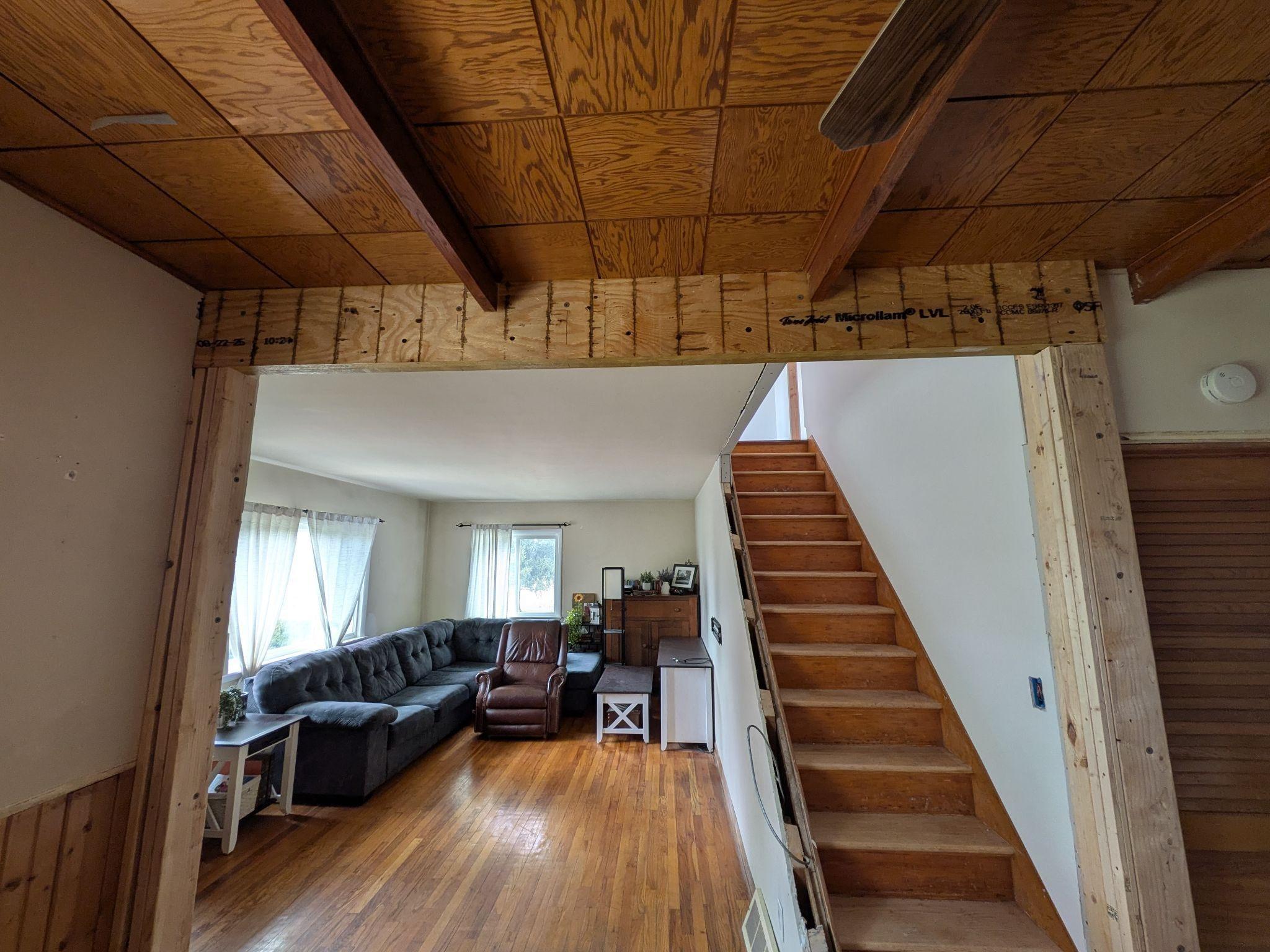 A finished living room with a wood ceiling, exposed beams, a staircase and a sectional sofa