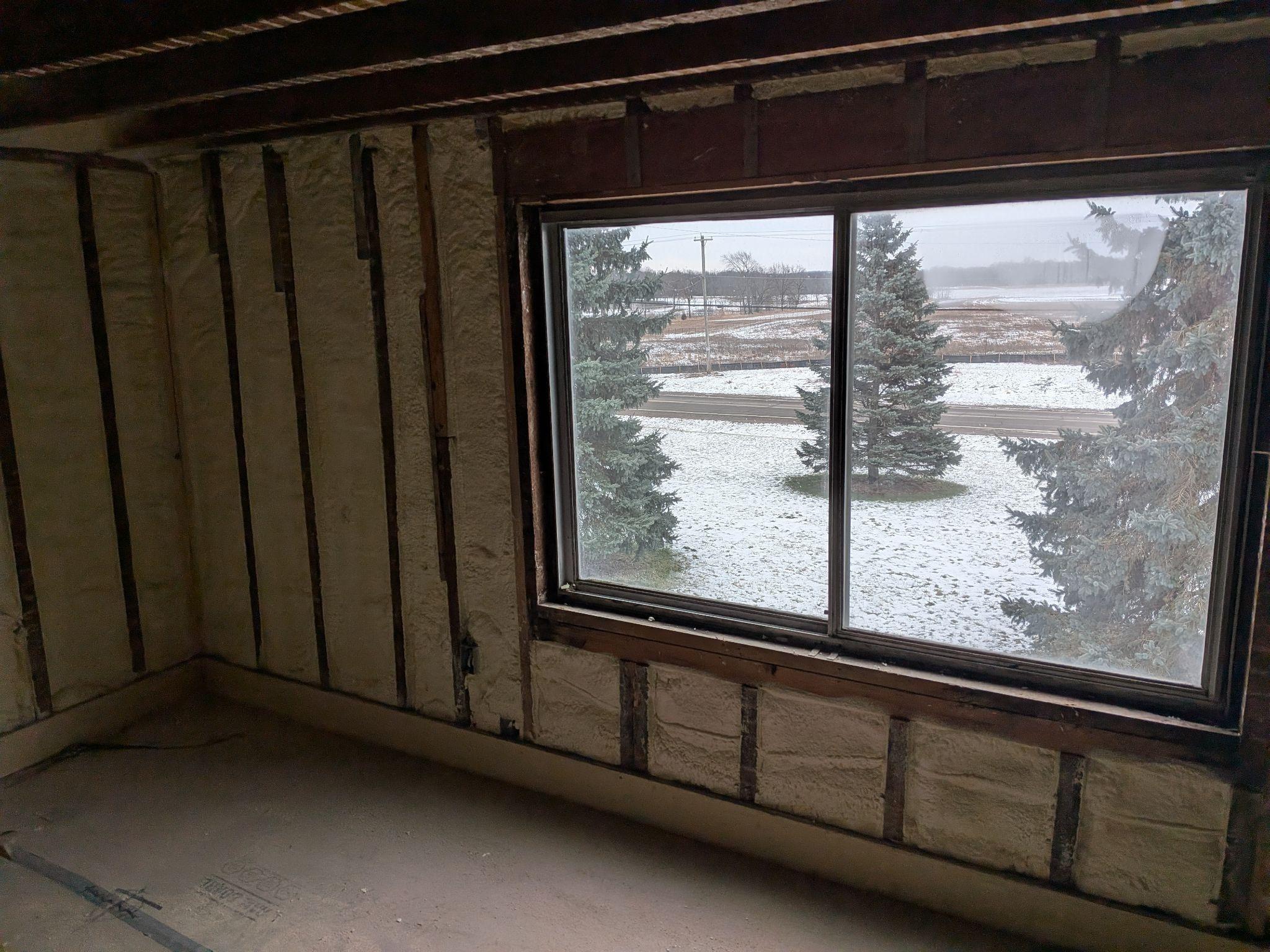 A room opened to the studs with insulation between them and a new window looking onto snow
