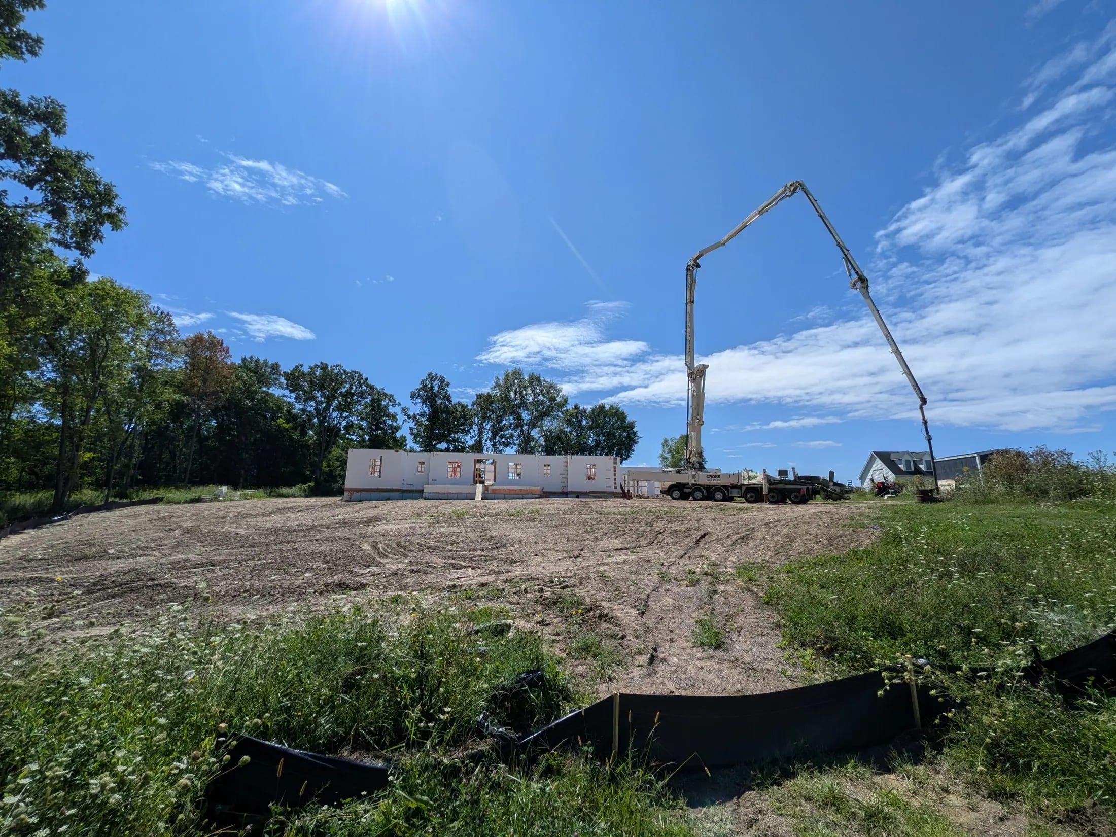 A concrete pump boom reaching over ICF walls on a cleared lot, seen from ground level